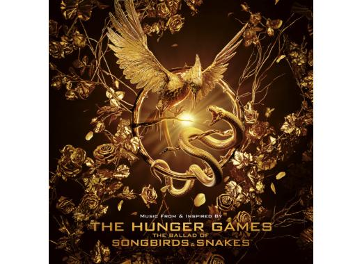 Image of a gold mockingjay landing on a gold circle with sticks. Wrapped around the gold circle is a gold serpent with it's fangs exposed. Around the mockingjay and serpent are several gold roses. 